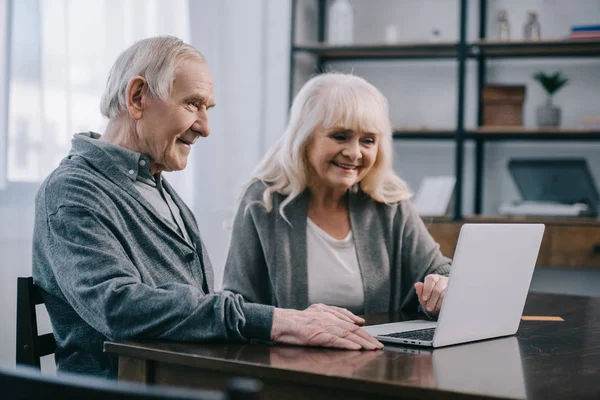 Sonriente Pareja Ancianos Sentado Mesa Uso Ordenador Portátil Casa — Foto de Stock