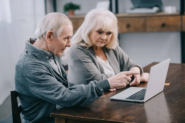 灰色头发的高级夫妇坐在桌子上 在家里使用笔记本电脑 — 图库照片