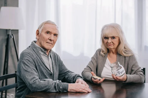 Triste Casal Sênior Sentado Mesa Olhando Para Câmera Segurando Frasco — Fotografia de Stock