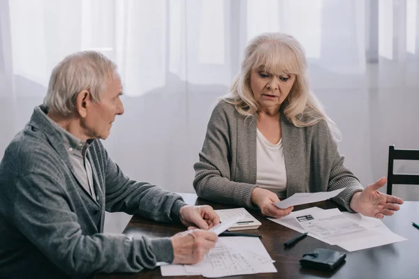 Surprised Senior Couple Casual Clothes Sitting Table Holding Bills Home — Stock Photo, Image