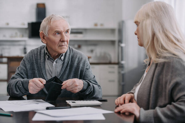 пожилая пара сидит за столом с документами и бумажником
