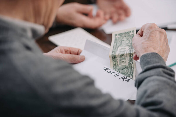 cropped view of man holding envelope with 'roth ira' lettering and dollar banknote