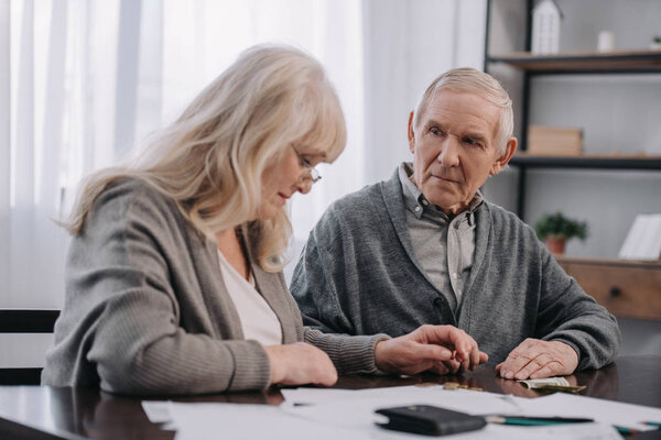 senior couple in casual clothes sitting at table with paperwork while counting money