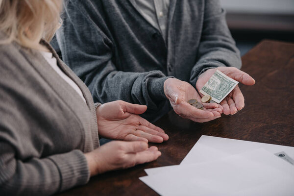 cropped view of senior couple sitting at table and holding money in hands
