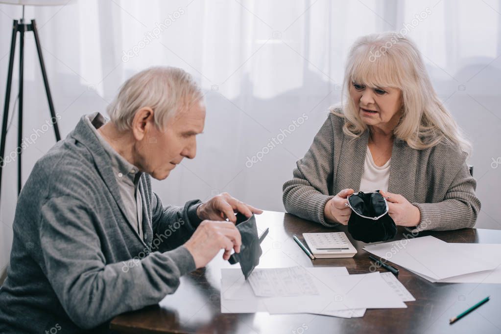 senior couple holding wallets while sitting at table with documents 