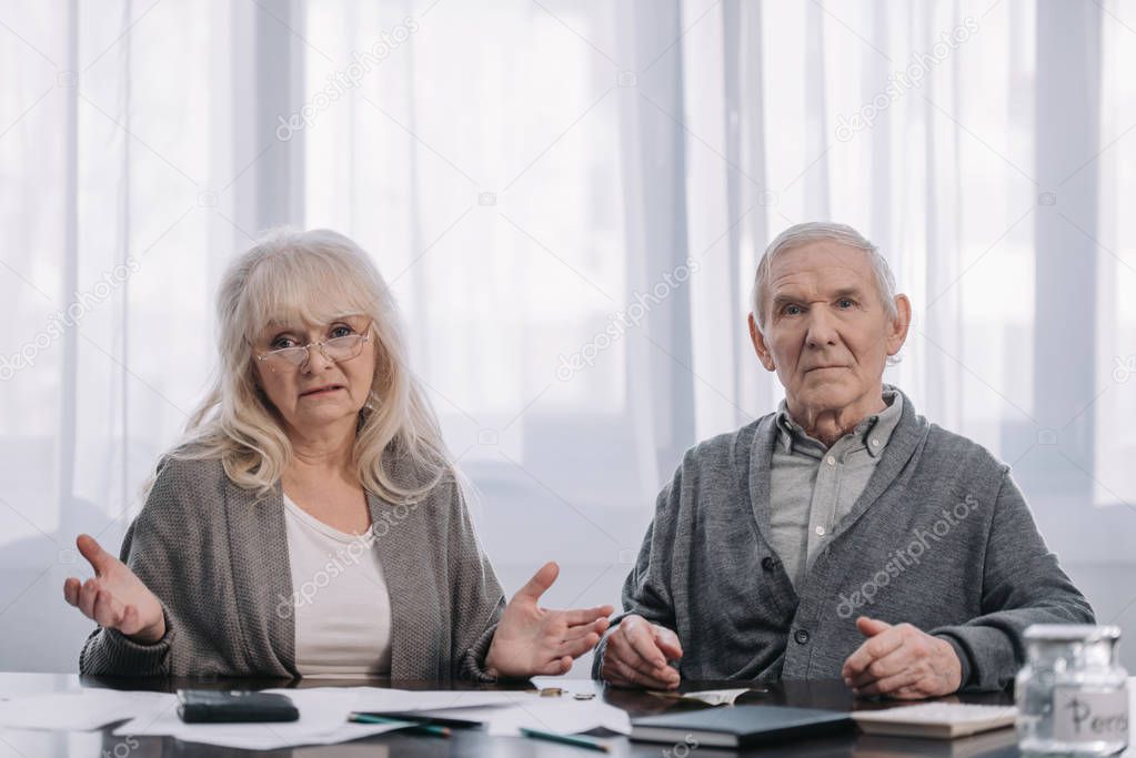 senior couple sitting at table with paperwork and looking at camera
