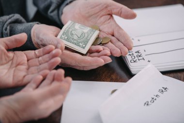 cropped view of couple holding money near envelope with 'roth ira' lettering and notebook clipart