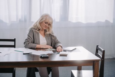 bütçe evde kopya alanı ile sayım sırasında para ve evrak ile masada oturan kadın kıdemli