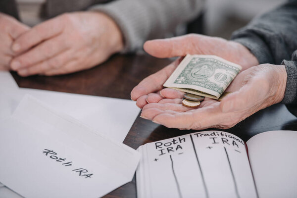 cropped view of couple holding money near envelope with 'roth ira' lettering and notebook
