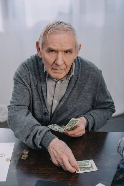 Старший Чоловік Сидить Столом Дивлячись Камеру Рахуючи Гроші Вдома — стокове фото