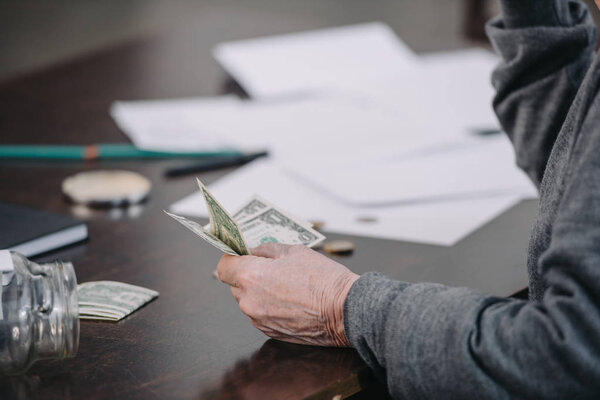 partial view of senior man sitting at table with paperwork and holding money