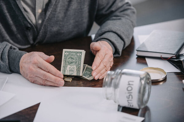partial view of senior man sitting at table and counting money at home