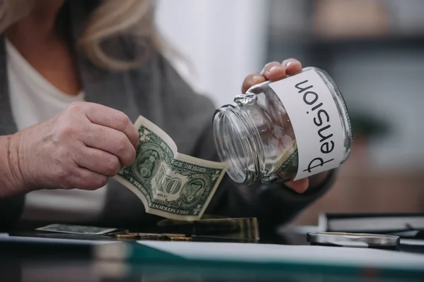 単語のドル紙幣とガラス瓶を保持している年配の女性のトリミング ビュー — ストック写真