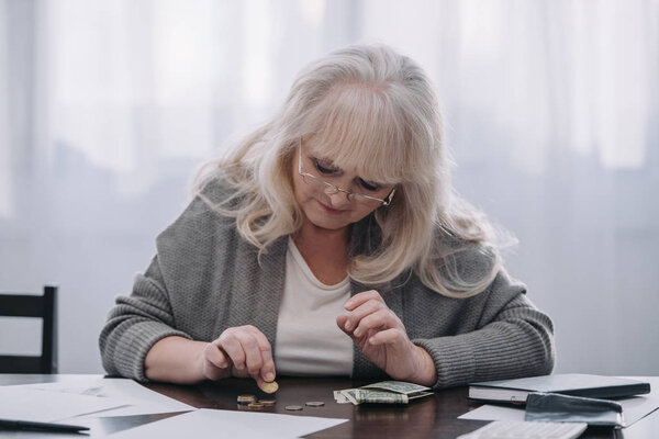 female pensioner sitting at table and counting money at home