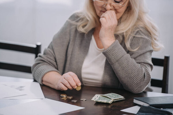 cropped view of female pensioner sitting at table and counting money at home