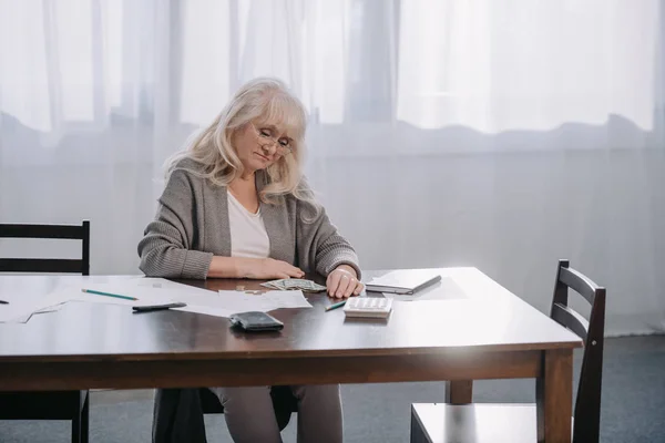 Senior Kobieta Siedzi Przy Stole Pieniędzy Dokumentów Podczas Liczenia Budżetu — Zdjęcie stockowe