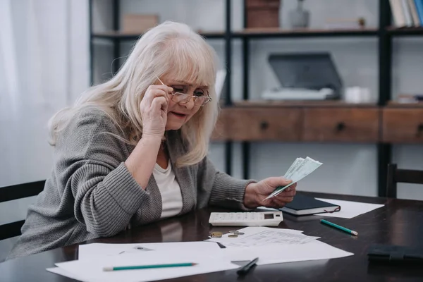 Senior Kobieta Siedzi Przy Stole Papierkową Robotę Trzymając Okulary Liczenie — Zdjęcie stockowe