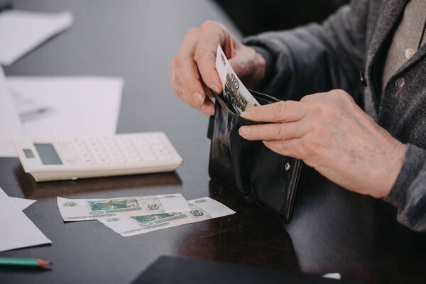 cropped view of male pensioner sitting at table and putting money in wallet 