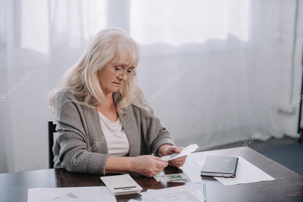 senior woman sitting at table with paperwork and counting money