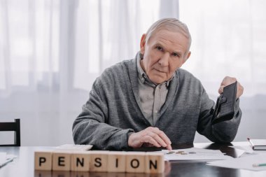 male pensioner with wallet and paperwork sitting at table with word 'pension' made of wooden blocks on foreground clipart
