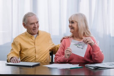 senior couple holding envelope with 'roth ira' lettering and money while sitting at table clipart