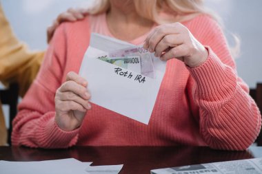 Kısmi görünümünü 'roth IRA' yazı ve para zarfı tutan kadın