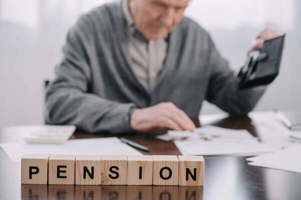 selective focus of word 'pension' made of wooden blocks with male pensioner holding wallet on background