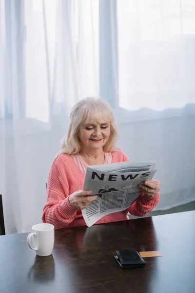 Ανώτερος Γυναίκα Κάθεται Στο Τραπέζι Και Διαβάζει Εφημερίδα Στο Σπίτι — Φωτογραφία Αρχείου