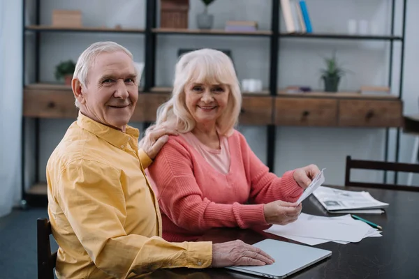 Glückliches Seniorenpaar Blickt Die Kamera Während Mit Dokumenten Tisch Sitzt — Stockfoto