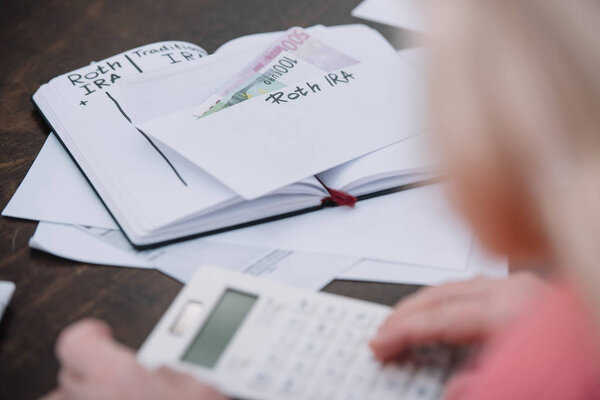 cropped view of senior woman, envelope with 'roth ira' lettering, money and notebook 