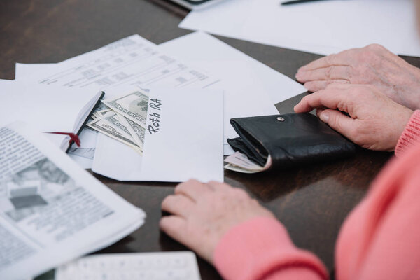 cropped view of senior couple sitting at table with paperwork, money and envelope with 'roth ira' lettering 