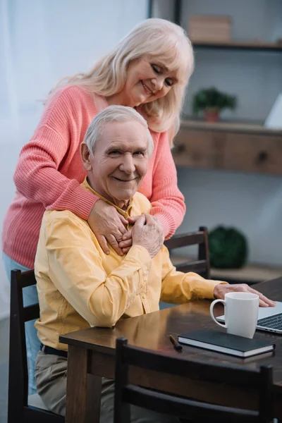 Senior Woman Hugging Smiling Man Sitting Table Looking Camera — Stock Photo, Image