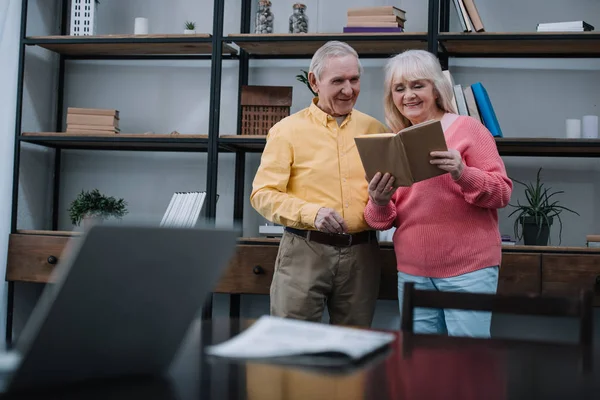 在客厅里穿着五颜六色的衣服阅读书的快乐的老夫妇的选择性焦点 — 图库照片