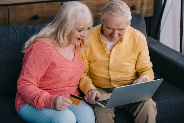 Pareja Ancianos Emocionados Sentado Sofá Con Ordenador Portátil Tarjeta Crédito —  Fotos de Stock