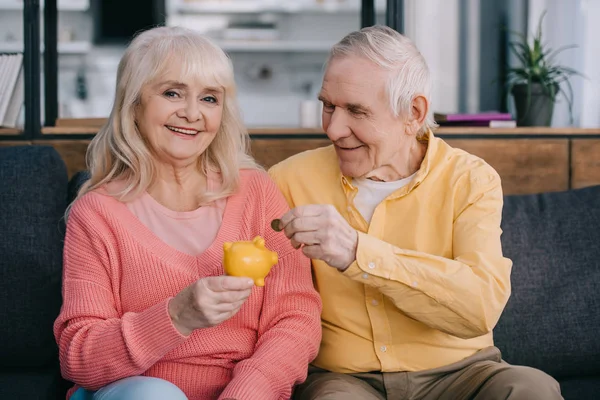 Casal Sênior Feliz Colocando Moeda Banco Piggy Amarelo — Fotografia de Stock