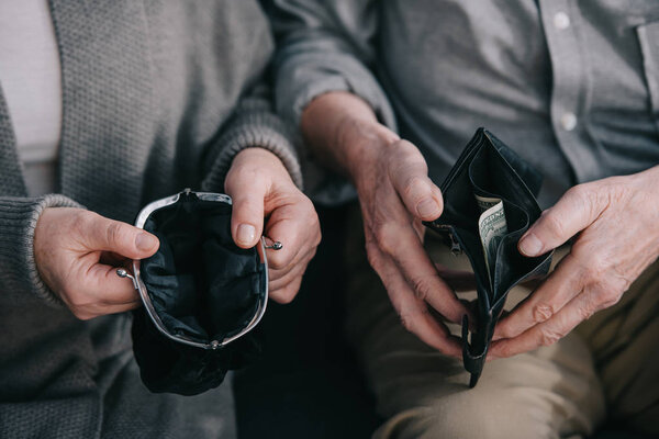 cropped view of senior couple sitting on couch and holding wallets at home