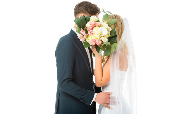 Невеста и жених обнимаются, скрывая лица за свадебным букетом, изолированным на белом
