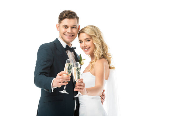 beautiful bride and handsome groom clinking glasses of champagne and looking at camera isolated on white