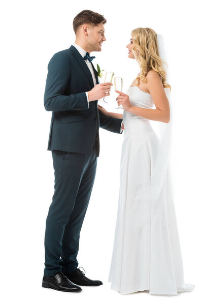 веселые невеста и жених звенящие бокалы шампанского и глядя друг на друга изолированы на белом
