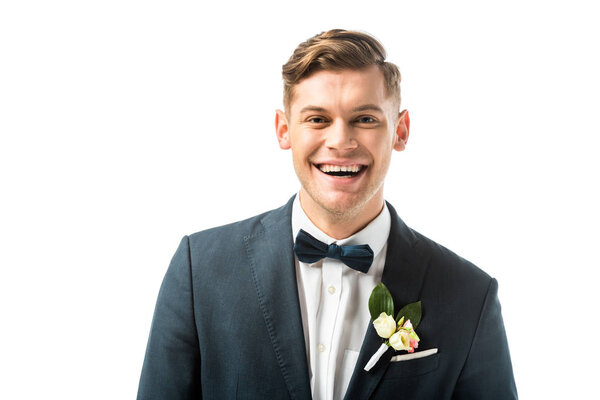 happy handsome bridegroom in bowtie and jacket with boutonniere looking at camera isolated on white