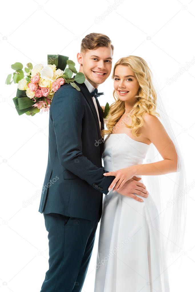 smiling bride with wedding bouquet hugging happy groom isolated on white