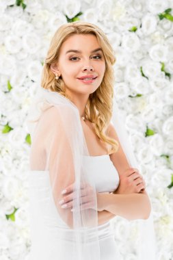 smiling beautiful bride with crossed hands looking at camera on white floral background clipart
