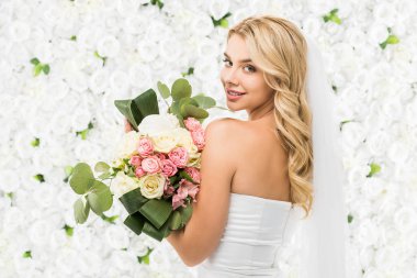 beautiful young bride holding wedding bouquet and looking at camera on white floral background clipart