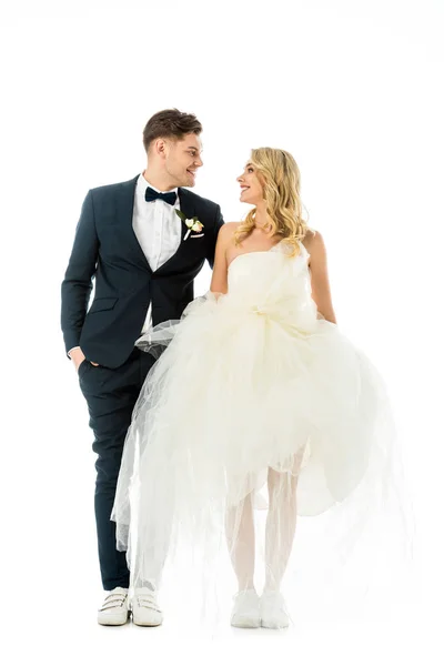 英俊的新郎和美丽的新娘在优雅的衣服和运动鞋看着对方孤立的白色 — 图库照片