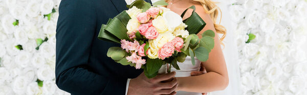 panoramic shot of bride and groom with wedding bouquet on white floral background