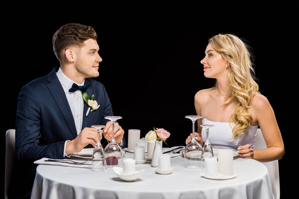 handsome groom and beautiful bride sitting at served table isolated on black