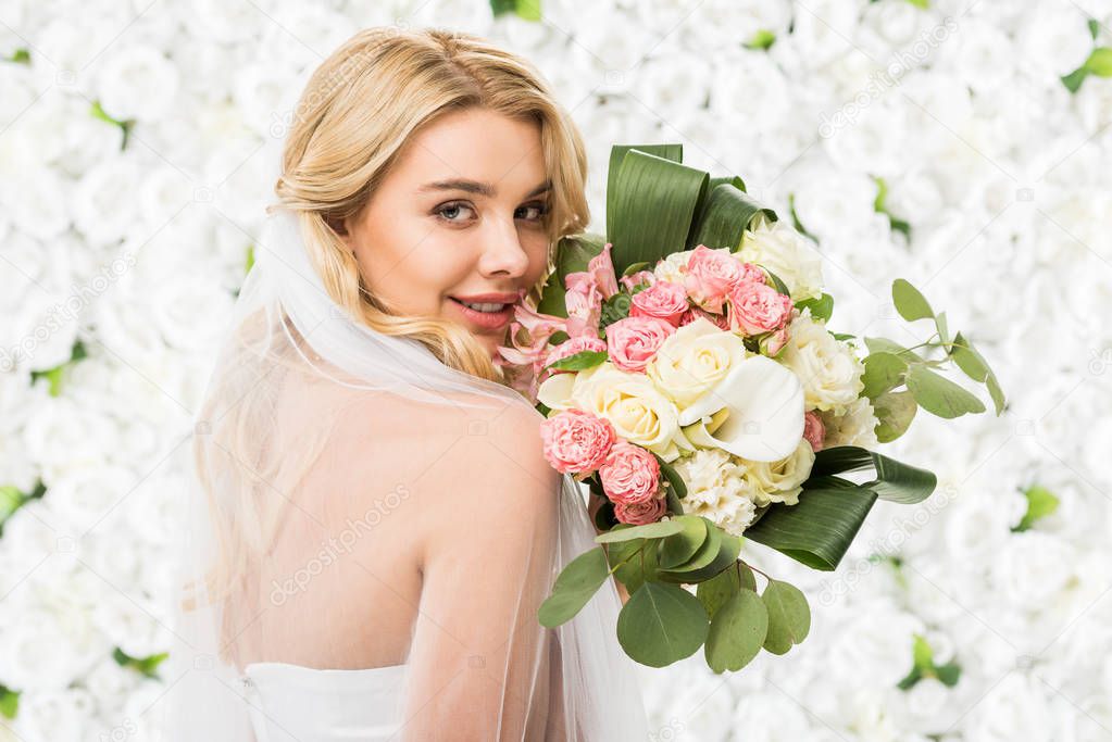 smiling attractive bride holding wedding bouquet on white floral background