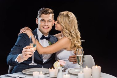 mutlu genç gelin kucaklayan yakışıklı damat siyah izole şampanya ile