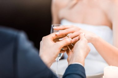 selective focus of man putting wedding ring on brides finger on black background clipart