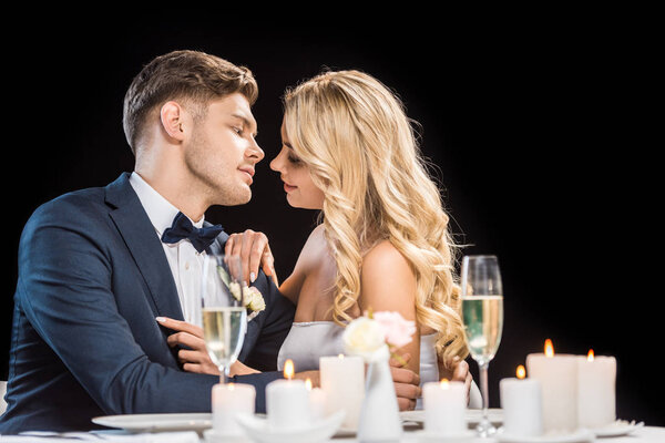happy couple hugging while sitting at served table isolated on black